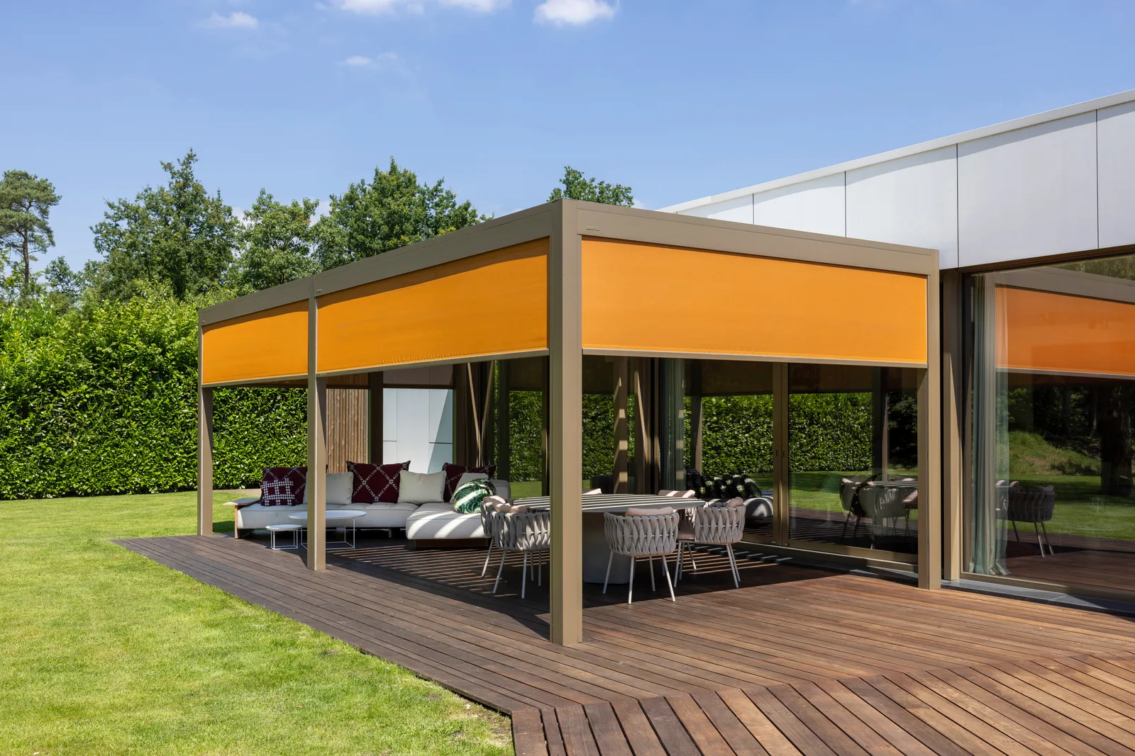 Lamellendach mit orangefarbenen Senkrechtmarkisen über einer Loungeterrasse auf Holzdeck