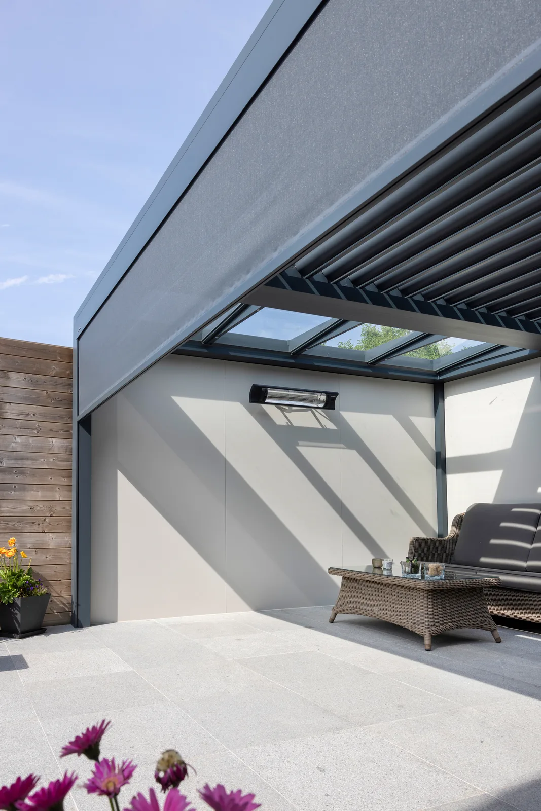 Lamellendach mit Glaselementen über einer Sitzecke an einer Terrassenwand