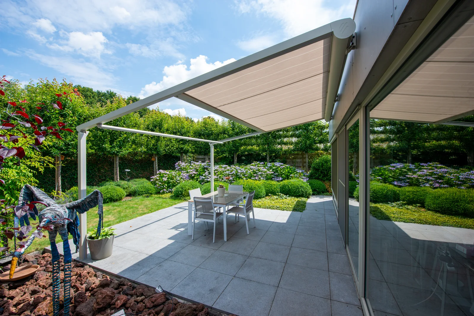 Beige Pergola-Markise über einer gepflasterten Terrasse mit Hortensien
