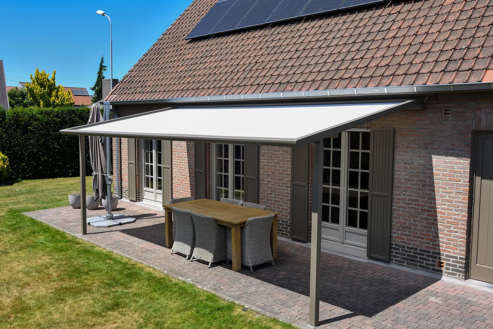 Weiße Pergola-Markise an einem Backsteinhaus über einem Terrassentisch