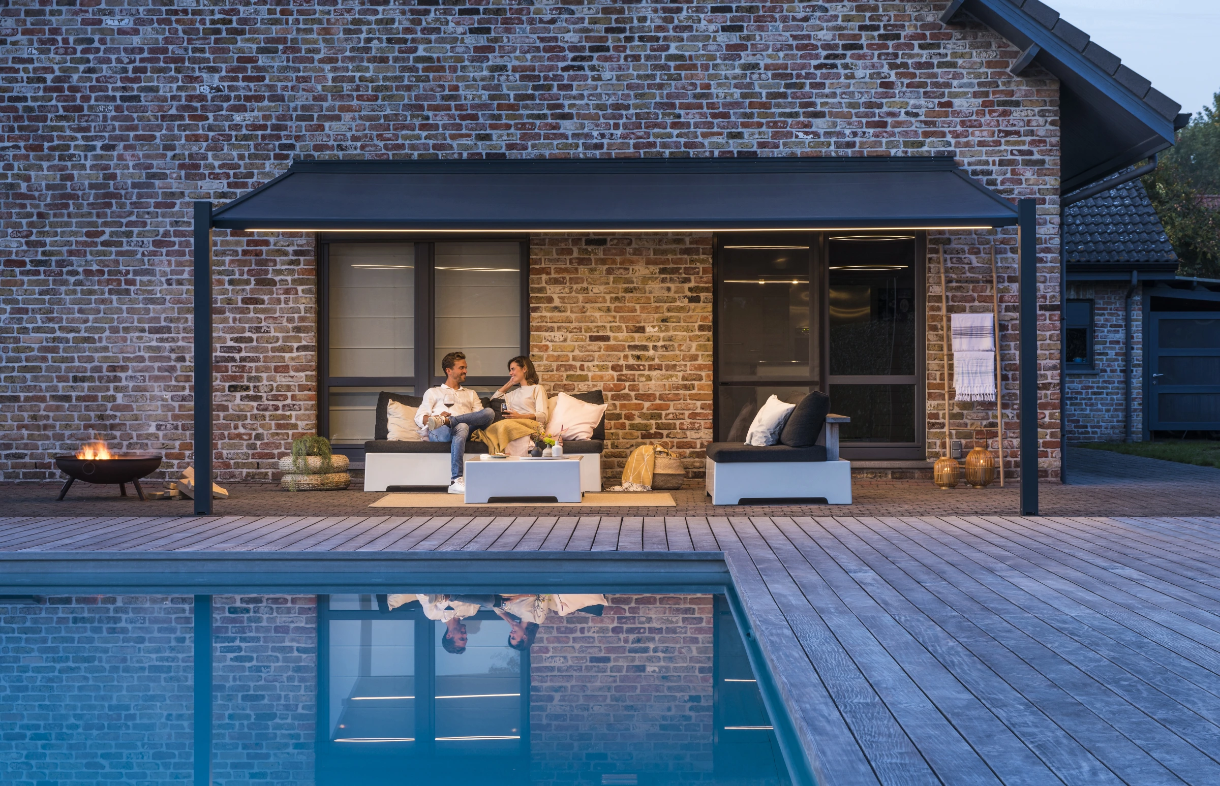 Pergola-Markise mit Lichtleiste über einer Lounge am Pool in der Abenddämmerung