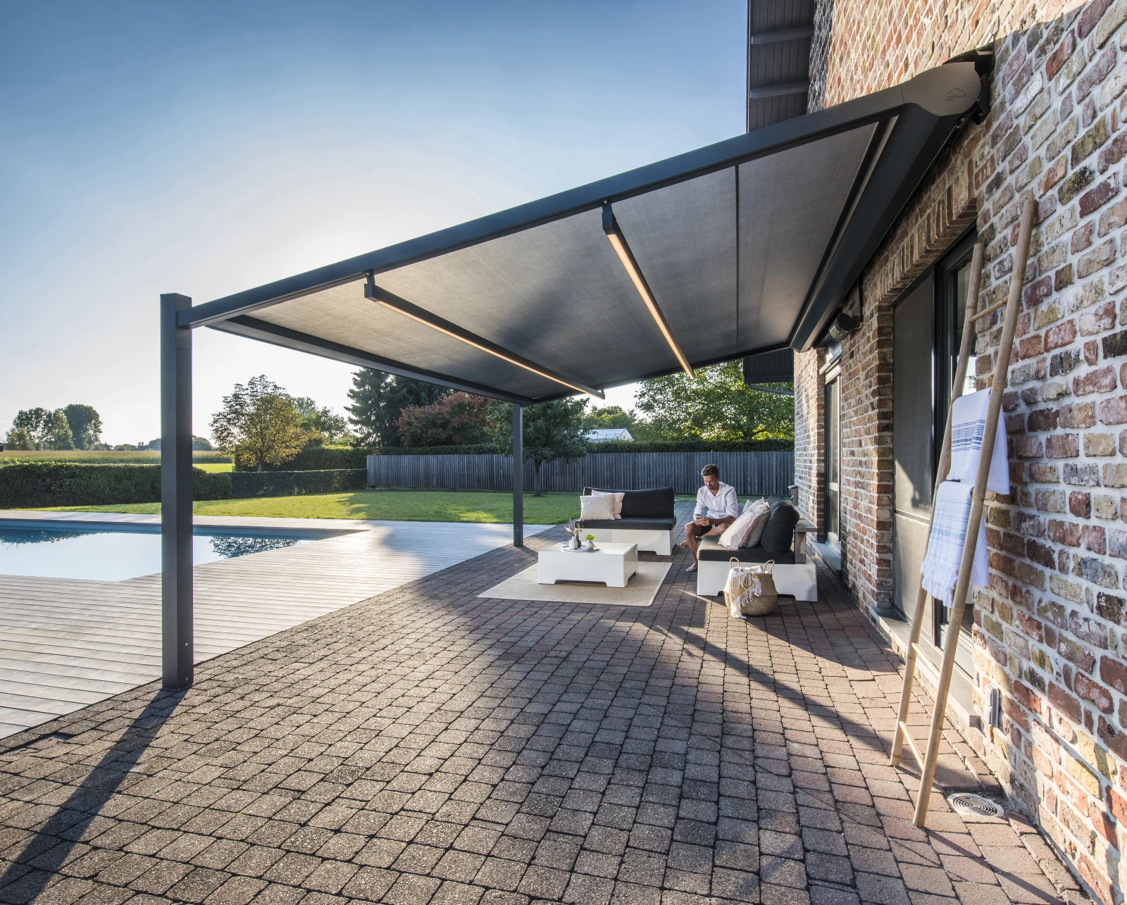 Freistehende Pergola-Markise mit dunklem Tuch und LED-Leisten über einer Lounge am Pool