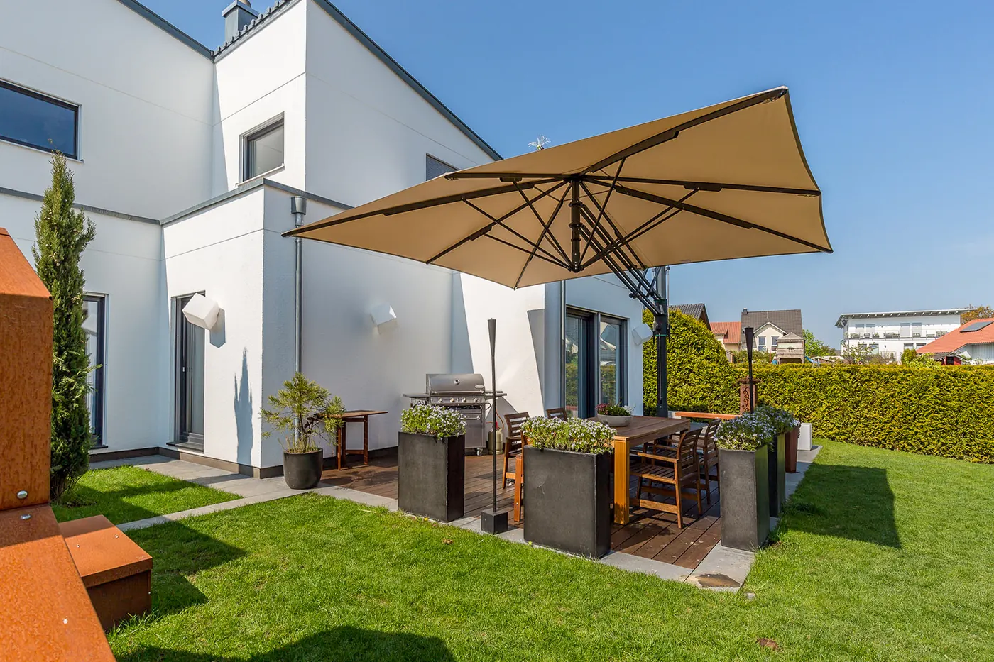 Freiarmschirm über einer Terrasse mit Sitzgruppe und Grill an einem modernen Wohnhaus