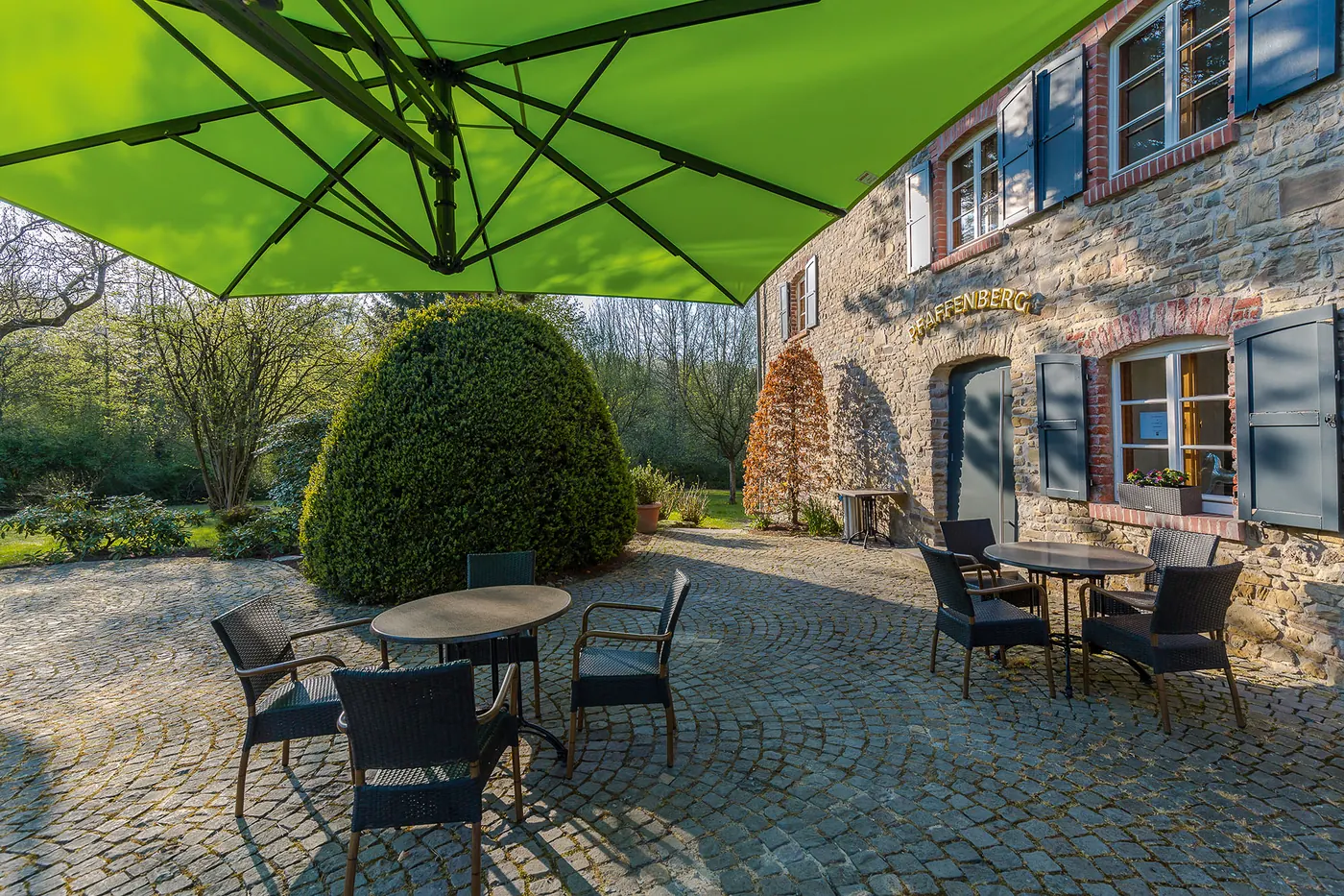 Freiarmschirm über einer Sitzgruppe vor einem Natursteinhaus